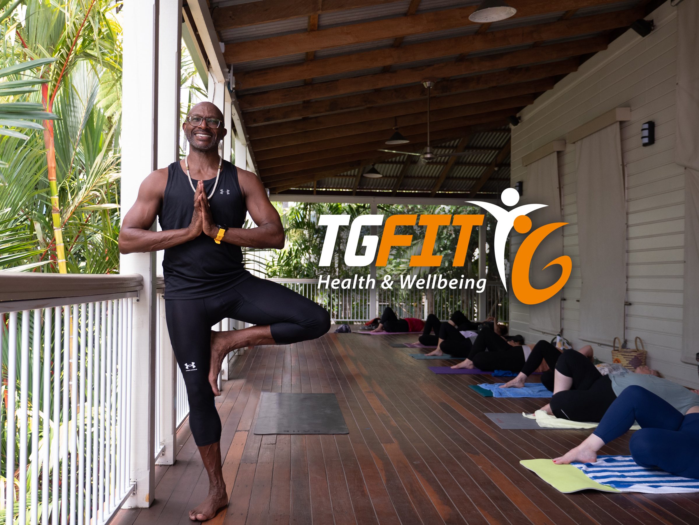 Welcome to TG FIT by Tony Grant. Image of Tony in tree pose on deck with yoga participants in background.